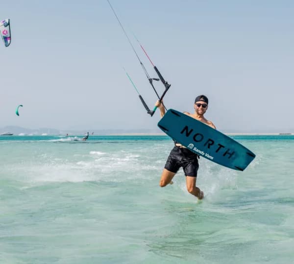 Kitesurfer riding shallow turquoise water beside a Red Sea sand island